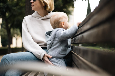 Young mother with her cute infant baby boy child sitting on bench in city parkの写真素材