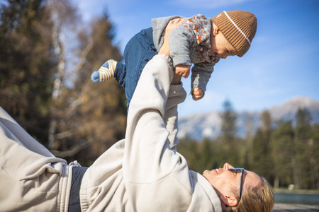 Happy family. Young mother playing with her baby boy infant oudoors on sunny autumn day. Portrait of mom and little son on wooden platform by lake. Positive human emotions, feelings, joyの写真素材
