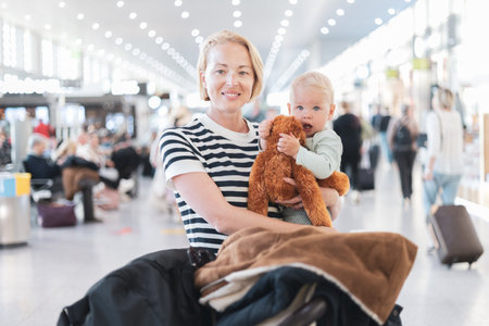 Mother traveling with child, holding his infant baby boy at airport terminal waiting to board a plane. Travel with kids conceptの写真素材