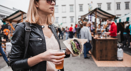 Close up of woman hands holding delicious organic salmon vegetarian burger and homebrewed IPA beer on open air beer an burger urban street food festival in Ljubljana, Sloveniaの写真素材