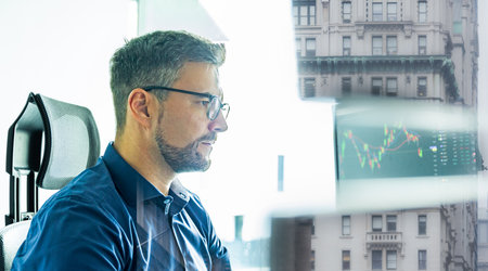 Male stock broker trading online watching charts and data analyses on multiple computer screens.の写真素材