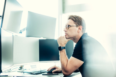 Male stock broker trading online watching charts and data analyses on multiple computer screens.の写真素材