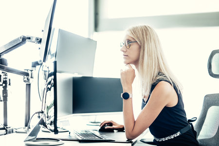 Female stock broker trading online watching charts and data analyses on multiple computer screensの写真素材