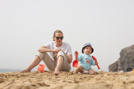Mother playing his infant baby boy son on sandy beach enjoying summer vacationson on Lanzarote island, Spain. Family travel and vacations conceptの写真素材