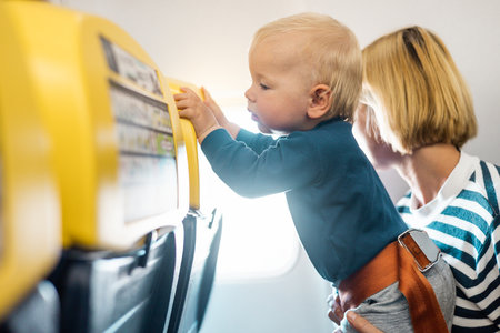 Mother and infant baby boy child flying on comercial flight, traveling by plane, sitting together at window seat. Flying with kidsの写真素材