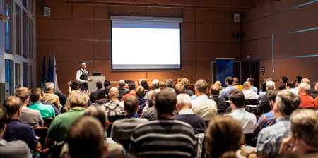 Speaker giving a talk in conference hall at business meeting event. Rear view of unrecognizable people in audience at the conference hall. Business and entrepreneurship concept.の写真素材