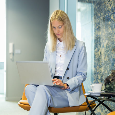 Beautiful business woman sitting at the table working on a laptop. Stylish woman in the modern office environmentの写真素材