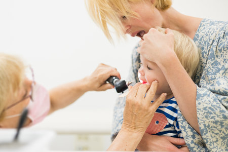 Infant baby boy child being examined by his pediatrician doctor during a standard medical checkup in presence and comfort of his mother. National public health and childs care care konceptの写真素材
