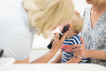 Infant baby boy child being examined by his pediatrician doctor during a standard medical checkup in presence and comfort of his mother. National public health and childs care care konceptの写真素材