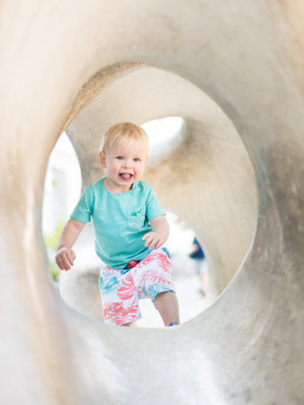 Child playing on outdoor playground. Toddler plays on school or kindergarten yard. Active kid on stone sculpured slide. Healthy summer activity for children. Little boy climbing outdoorsの写真素材