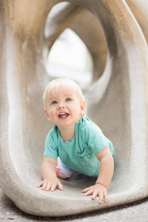Child playing on outdoor playground. Toddler plays on school or kindergarten yard. Active kid on stone sculpured slide. Healthy summer activity for children. Little boy climbing outdoorsの写真素材