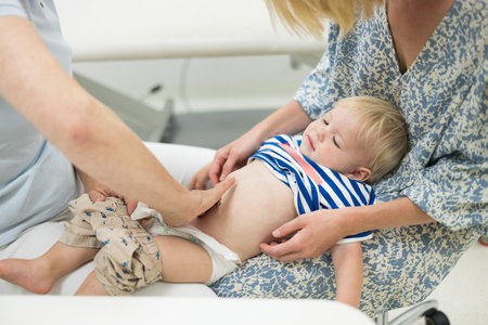 Infant baby boy child being examined by his pediatrician doctor during a standard medical checkup in presence and comfort of his mother. National public health and childs care care konceptの写真素材
