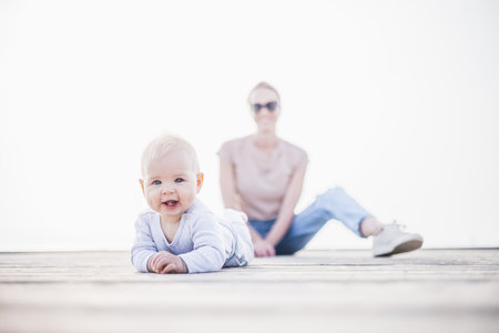 Happy family. Young mother playing with her baby boy infant oudoors on sunny autumn day. Portrait of mom and little son on wooden platform by lake. Positive human emotions, feelings, joyの写真素材