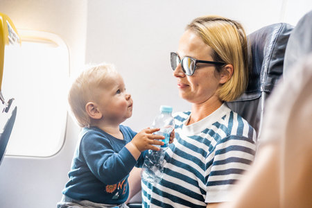 Mom and child flying by plane. Mother holding and playing with her infant baby boy child in her lap during economy comercial flight. Concept photo of air travel with baby. Real peopleの写真素材