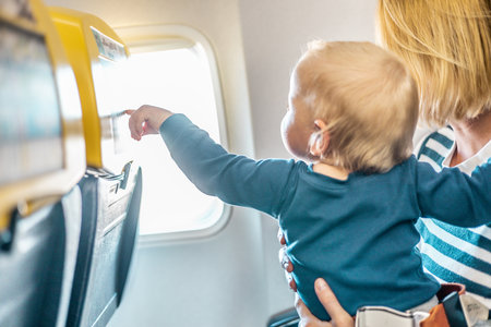 Mom and child flying by plane. Mother holding and playing with her infant baby boy child in her lap during economy comercial flight. Concept photo of air travel with baby. Real peopleの写真素材