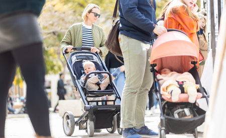 Mother walking and pushing his infant baby boy child in stroller in crowd of people wisiting sunday flea market in Malaga, Spainの写真素材