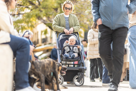 Mother walking and pushing his infant baby boy child in stroller in crowd of people wisiting sunday flea market in Malaga, Spainの写真素材