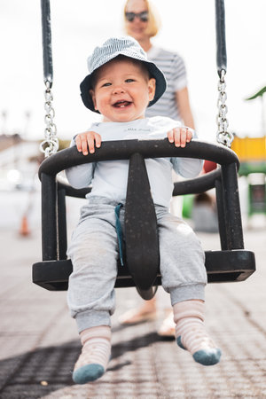 Mother pushing her infant baby boy child on a swing on playground outdoorsの写真素材