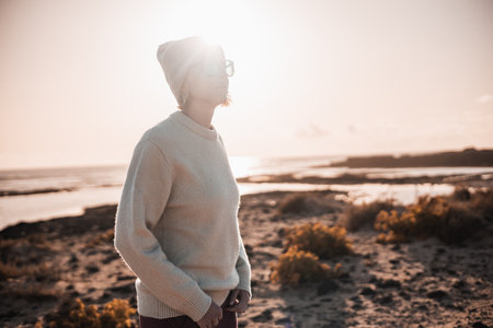 Portrait of young stylish woman wearing wool sweater, wool cap and sunglasses on long sandy beach in springの写真素材