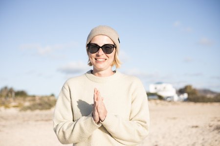Portrait of young stylish woman wearing wool sweater, wool cap and sunglasses on long sandy beach in spring.の写真素材