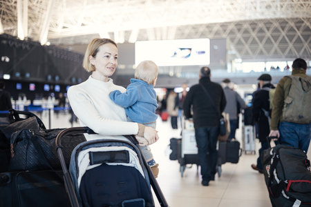 Motherat travelling with his infant baby boy child, walking, pushing baby stroller and luggage cart at airport terminal station. Travel with child conceptの写真素材