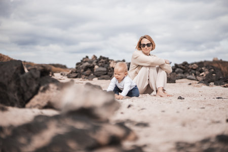 Mother enjoying winter beach vacations playing with his infant baby boy son on wild volcanic sandy beach on Lanzarote island, Canary Islands, Spain. Family travel and vacations concept.の写真素材