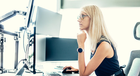 Female financial assets manager, trading online, watching charts and data analyses on multiple computer screens. Modern corporate business woman concept.の写真素材