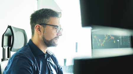 Male stock broker trading online watching charts and data analyses on multiple computer screens.の写真素材