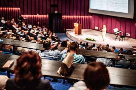Business and entrepreneurship symposium. Female speaker giving a talk at business meeting. Audience in conference hall. Rear view of unrecognized participant in audience.の写真素材