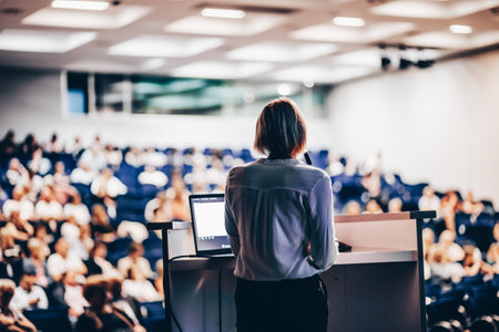 Female speaker giving a talk on corporate business conference. Unrecognizable people in audience at conference hall. Business and Entrepreneurship eventの写真素材