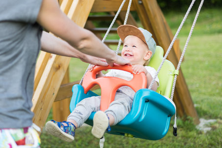 Mother pushing her infant baby boy child on a swing on playground outdoorsの写真素材