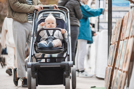 Mother walking and pushing his infant baby boy child in stroller in crowd of people wisiting sunday flea market in Malaga, Spainの写真素材