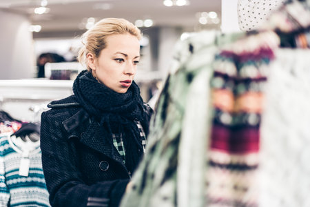 Woman shopping clothes. Shopper looking at clothing indoors in store. Beautiful blonde caucasian female model.の写真素材