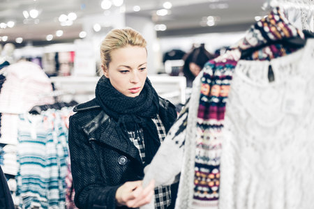 Woman shopping clothes. Shopper looking at clothing indoors in store. Beautiful blonde caucasian female model.の写真素材
