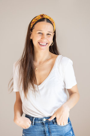 Portrait of confident beautiful woman with long brown hair, wearing casual clothes, standing in relaxed pose with hands in pockets, smiling with white teeth at camera, studio backgroundの写真素材