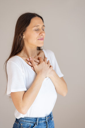 Woman with hands on chest doing breathing exercise at homeの写真素材