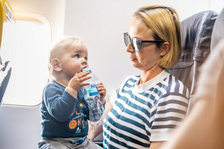 Mom and child flying by plane. Mother holding and playing with her infant baby boy child in her lap during economy comercial flight. Concept photo of air travel with baby. Real peopleの写真素材