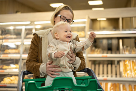Caucasian mother shopping with her infant baby boy child choosing products in department of supermarket grocery storeの写真素材
