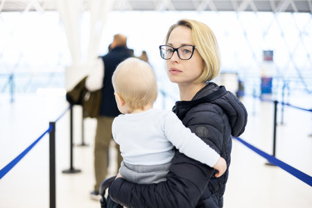 Mother holding his infant baby boy child queuing at airport terminal in passport control line at immigrations departure before moving to boarding gates to board an airplane. Travel with baby concept.の写真素材