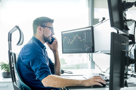 Male stock broker trading online watching charts and data analyses on multiple computer screens.の写真素材