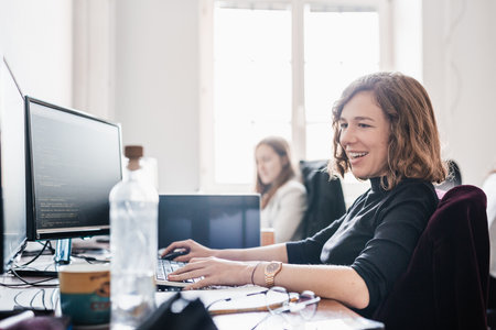 Women in startup business and entrepreneurship. Yound devoted female AI programmers and IT software developers team programming on desktop computer in startup company share office space.の写真素材