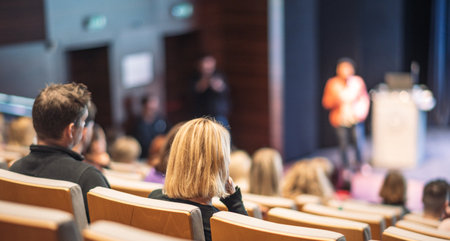 Business and entrepreneurship symposium. Female speaker giving a talk at business meeting. Audience in conference hall. Rear view of unrecognized participant in audience.の写真素材