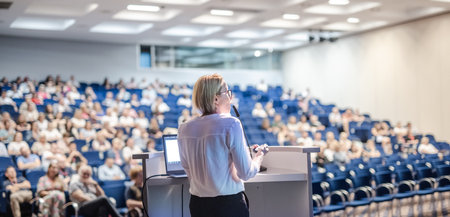 Female speaker giving a talk on corporate business conference. Unrecognizable people in audience at conference hall. Business and Entrepreneurship eventの写真素材