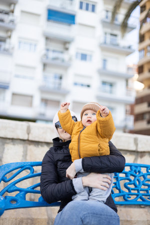 Young mother with her cute infant baby boy child on bench in city parkの写真素材