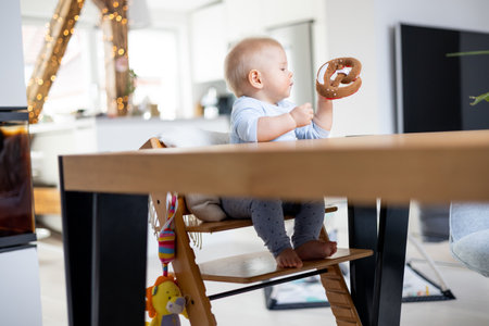 Happy infant sitting at dining table and playing with his toy in traditional scandinavian designer wooden high chair in modern bright atic home. Cute baby playing with toys.の写真素材