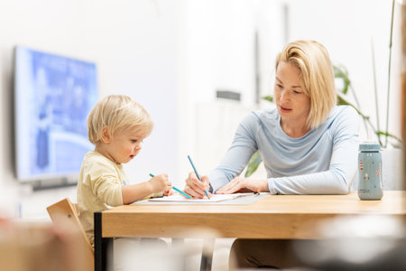 Caring young Caucasian mother and small son drawing painting in notebook at home together. Loving mom or nanny having fun learning and playing with her little 1,5 year old infant baby boy childの写真素材