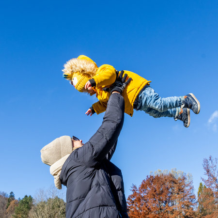 More, more,...mum, thats fun. Happy young mother throws her cute little baby boy up in the air. Mothers Day, Mather and her son baby boy playing and hugging outdoors in nature in fallの写真素材