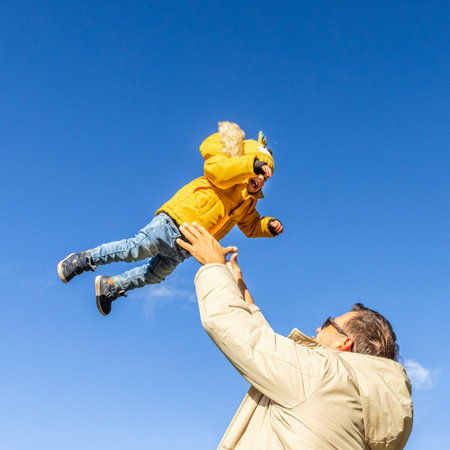 More, more,... dad, thats fun. Happy young father throws his cute little baby boy up in the air. Fathers Day, Father and his son baby boy playing and hugging outdoors in nature in fallの写真素材