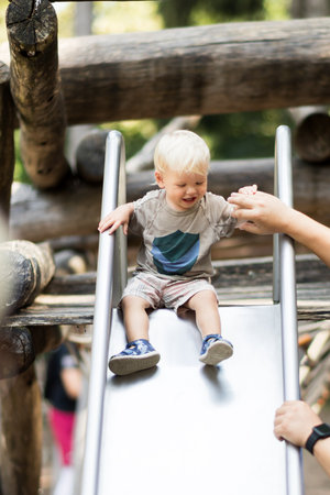 Parent hand holding little infant baby boy child while sliding on urban playground on a sunny summer day. Family joy and happiness concept.の写真素材