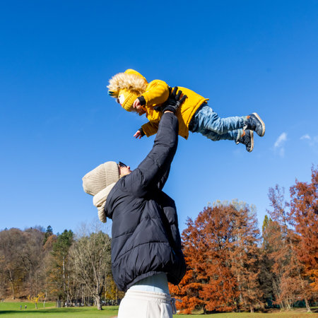 More, more,...mum, thats fun. Happy young mother throws her cute little baby boy up in the air. Mothers Day, Mather and her son baby boy playing and hugging outdoors in nature in fallの写真素材